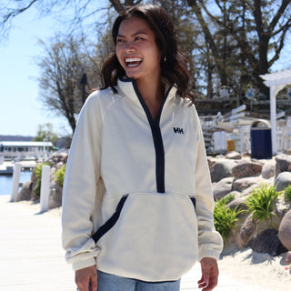 Woman wearing a white fleece jacket with a brand logo by a lakeside setting